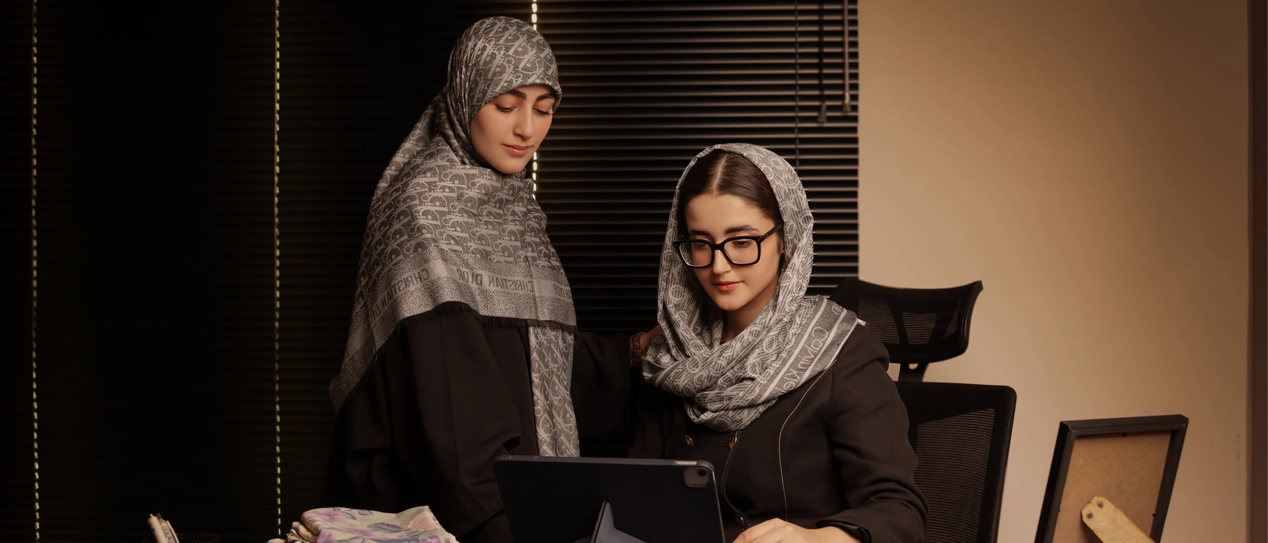 خانمی با روسری طرح‌دار و عینک، نشسته روی مبل چرمی به همراه تبلت