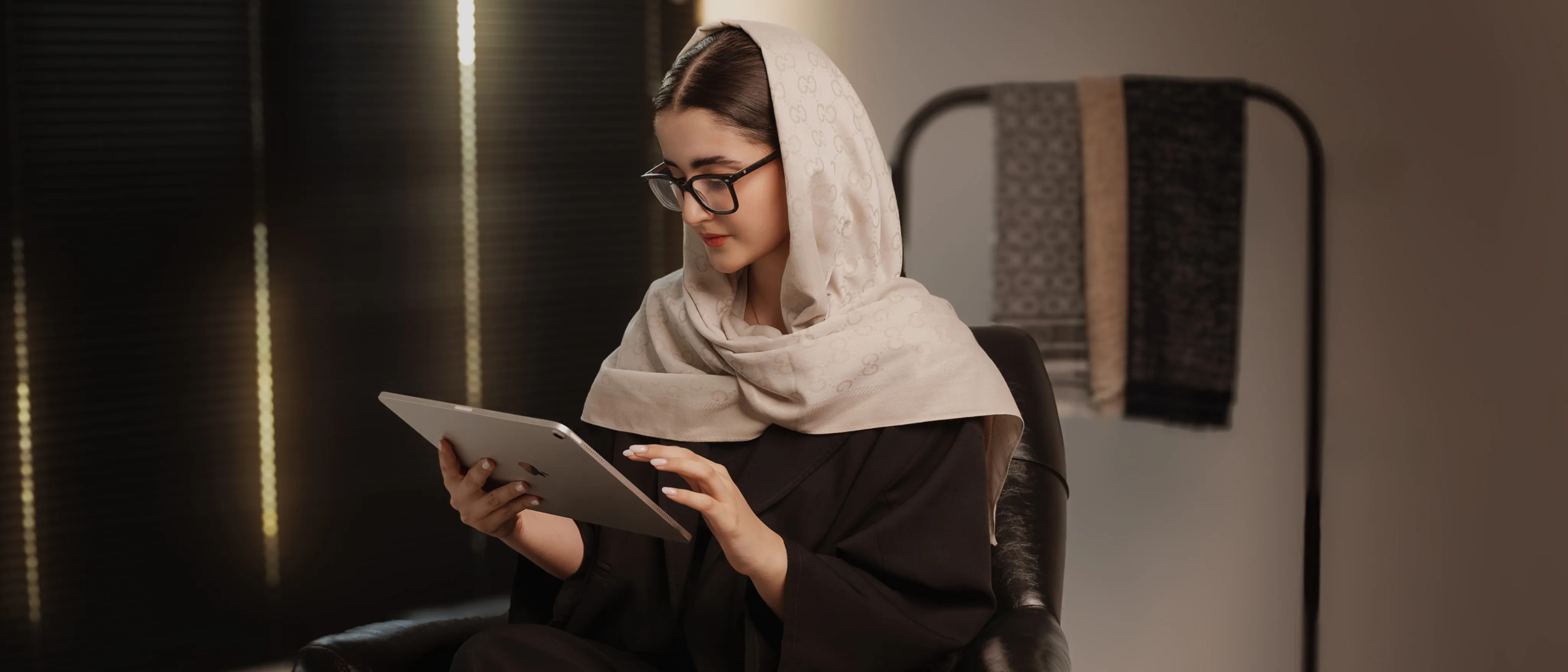 خانمی با روسری بژ طرح‌دار و عینک در حال استفاده از تبلت